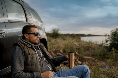 Young man is drinking tea while fishing. Outdoor picnic concept