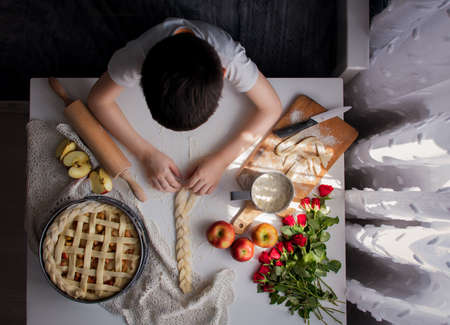 Cooking apple pie. The boy is kneading raw dough to make a pie. The child decorates the pie.の写真素材