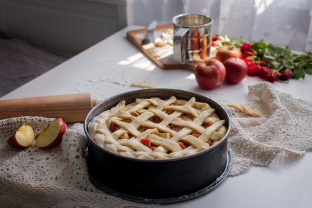 an apple pie is on the table, a rolling pin lies nearby, the sun is shining from the windowの写真素材