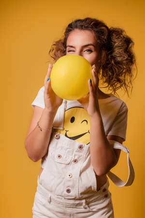 girl inflates a balloon on a yellow background .Young beautiful girl inflating a yellow balloon isolated on a yellow background. close-up image. The concept of youth, joy and fun.の写真素材