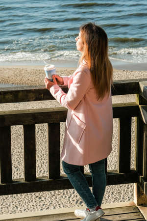 beautiful girl walking on the seashore with coffee .Beautiful girl is walking by the sea with coffee. blonde. Cheerful girl with beautiful hair in the sun. sea.の写真素材