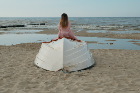 thoughtful girl sits on the seashore. girl on an overturned boat..の写真素材
