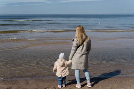 child with mom playing on the seashore in cold weather..の写真素材