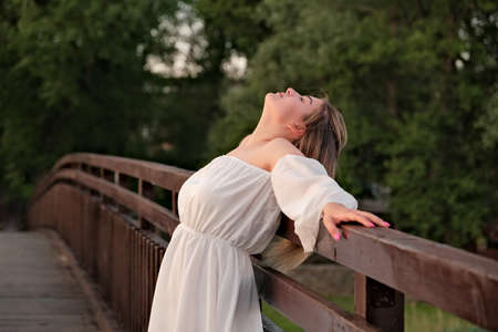 a beautiful girl in a white dress stands on a wooden bridge.の写真素材