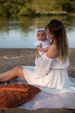 mom with a newborn baby sits on the beach, on the sand. mom holds a newborn baby in her arms.の写真素材