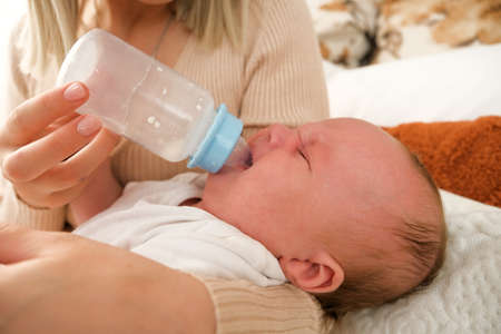 mom feeds a newborn baby with a bottle. the sun is shining in the background.