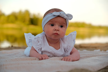 newborn baby girl lies on the beach. in a white dress.
