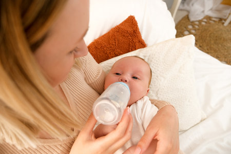 mom feeds a newborn baby with a bottle. the sun is shining in the background.