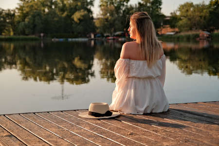 a beautiful girl in a hat stands on the shore. hat in hand.の写真素材