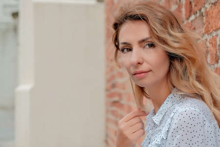 a beautiful girl stands against the background of a brick wall. the girl points her gaze at the advertisement.の写真素材