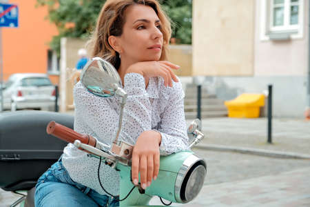 a beautiful girl sits on a city moped. the girl points her gaze at the advertisement.