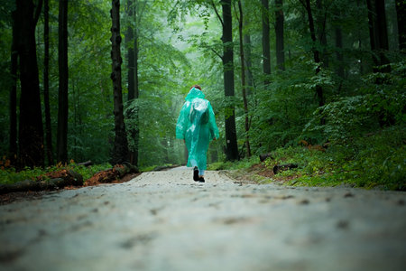 a girl tourist in a raincoat walks through the forest. forest with path.の写真素材
