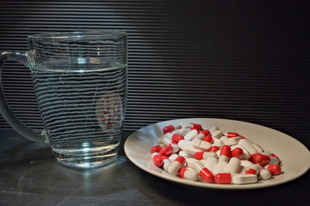 white and red pills in a plate. a glass of water. close up. the concept of health, treatment.