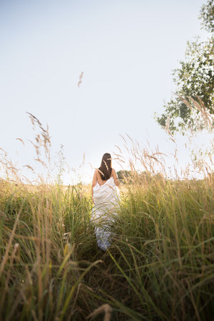 Young woman in white dress standing in grass field at sunny day.の写真素材