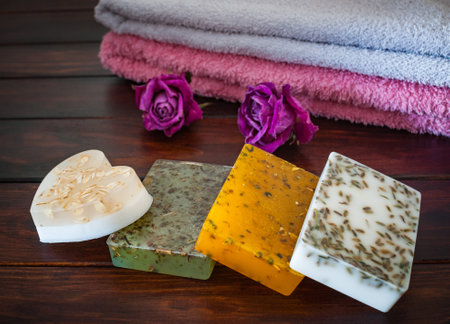 Handmade soap on a wooden table with towels and roses.