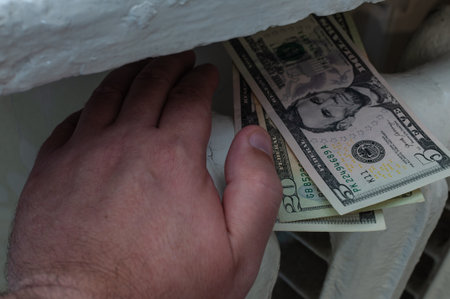A hand lying on a radiator with American dollar bills symbolizes the lack of heat and cold radiators...