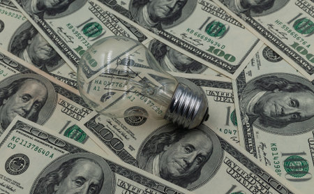 A light bulb against a background of hundred-dollar bills. A concept for saving on electricity.の写真素材