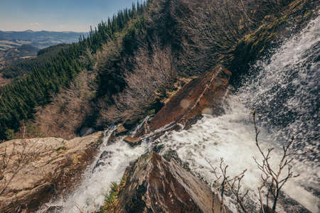 A waterfall with trees on the side of a mountainの写真素材