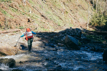 Mountains, river, tourist with a backpack crosses the riverの写真素材