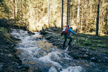River in the mountains with stones, a tourist crosses the river