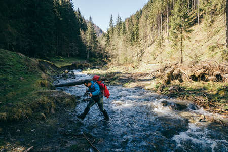 Mountains, river, man with a backpack crosses the riverの写真素材