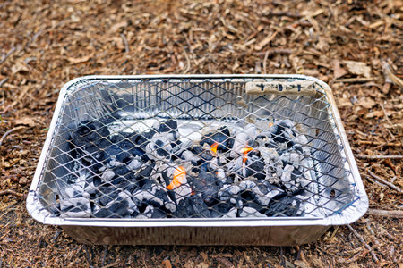 Disposable foil grill with burning charcoal.
