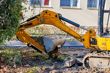 Part of a yellow, tracked mini excavator with a bucket in front of a building. High quality photoの写真素材
