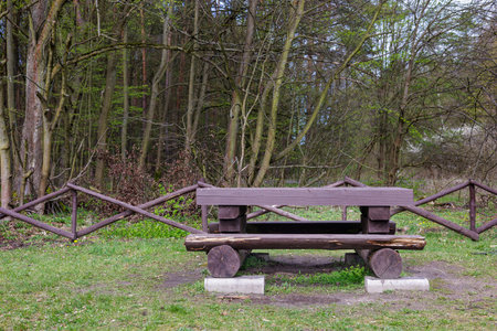 Wooden bench made of logs against the background of the forest. Recreation area near the forest.