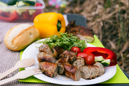 Sliced ââfried sausages lie on a plate with tomatoes, paprika, herbs and bread. Outdoor picnic.の写真素材