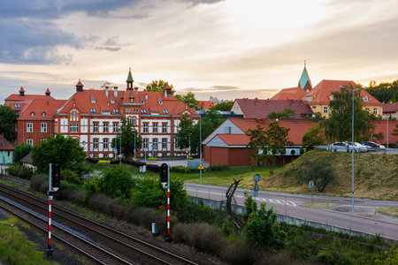 An old building with turrets under a red tiled roof next to a railway. Cityscape with a sunset sky.
