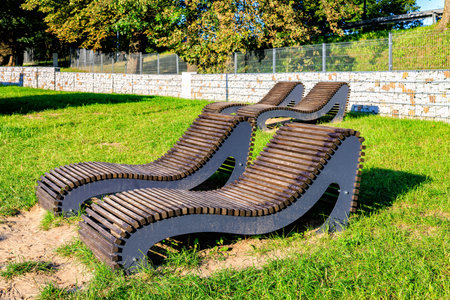 Four stationary wooden sun loungers arranged in pairs on the city beach. Green lawn. Gobion fencing.の写真素材