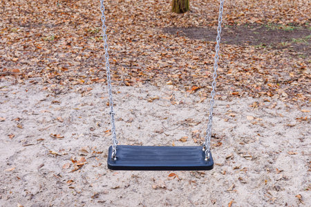 The black plastic seat of the swing is suspended by chains. Swing seat without a child against the background of yellow leaves. High quality photoの写真素材