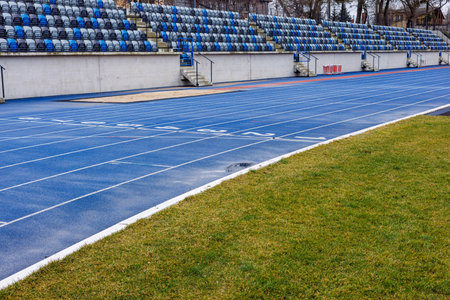 Blue running tracks with numbers. Plastic folding seats at the city stadium. Blue and gray seats in...