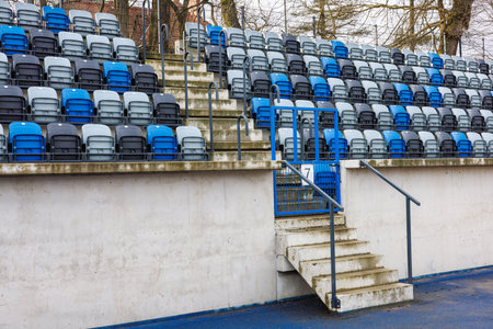Rows of blue and gray numbered seats in a stadium near an aisle with concrete steps. High quality...