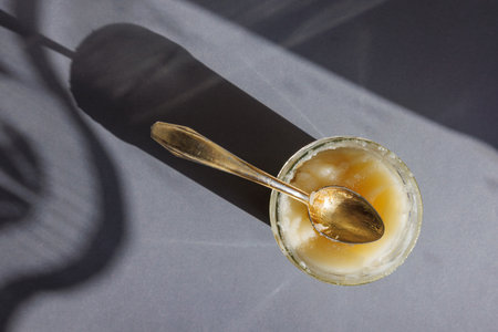 Jar of raw crystallized honey with spoon on grey background with sharp shadows. Organic food. Top view.の写真素材