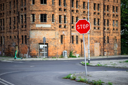 A tilted red STOP sign at an intersection against the backdrop of an old windowless building. The...