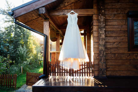 A beautiful cream wedding dress hanging on the wall near the wooden houseの写真素材