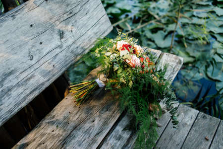 Lush wedding bouquet on a gray wooden bench near the water with water lilyの写真素材