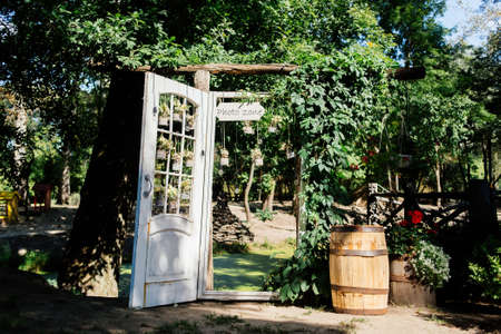 Wedding arch with white door overgrown with ivy and decorated with flowers  in jars and lights. Wedding rustic photozone.の写真素材