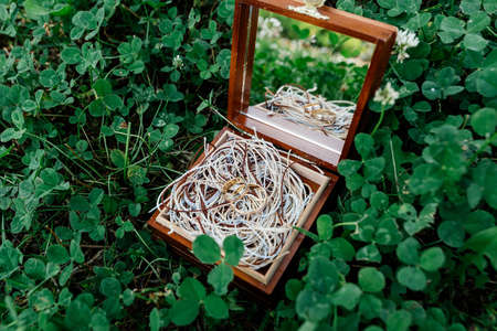 Golden wedding rings lie on the ropes in a wooden box with a mirror, which stands on the grass.の写真素材