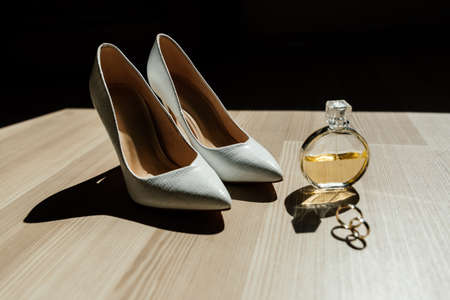 Bride's shoes, perfume and wedding rings are on the tableの写真素材