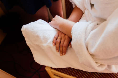A girl in a white robe sits on a chair and crosses her hands on her kneesの写真素材