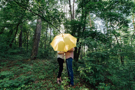 ?ouple in love under a yellow umbrella in a forest