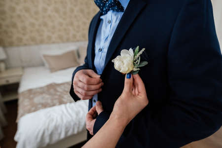Bride inserting the boutonniere in buttonhole of man in suit
