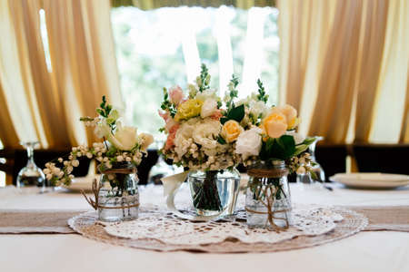 Wedding bouquets of yellow, white and pink roses are in vases on dinner tableの写真素材