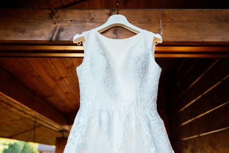 A beautiful cream wedding dress hanging on the wall near the wooden houseの写真素材