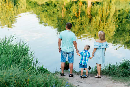 Mother, father and son holding hands on the river bank. Happy young family spending time on the bank of the river on a warm summer dayの写真素材