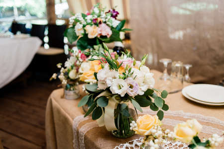 Wedding bouquets of yellow, white and pink roses are in vases on dinner tableの写真素材