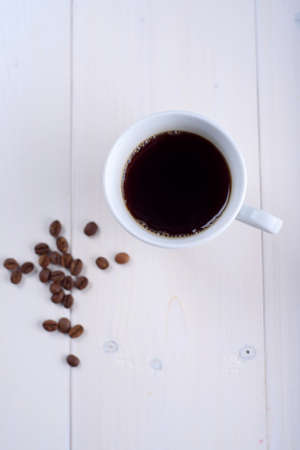 Coffee in a white cup on a white background. Coffee beans on the tableの写真素材