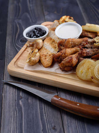 Fried meat slices of chicken wings, ham, fillets with sauce on a wooden boardの写真素材
